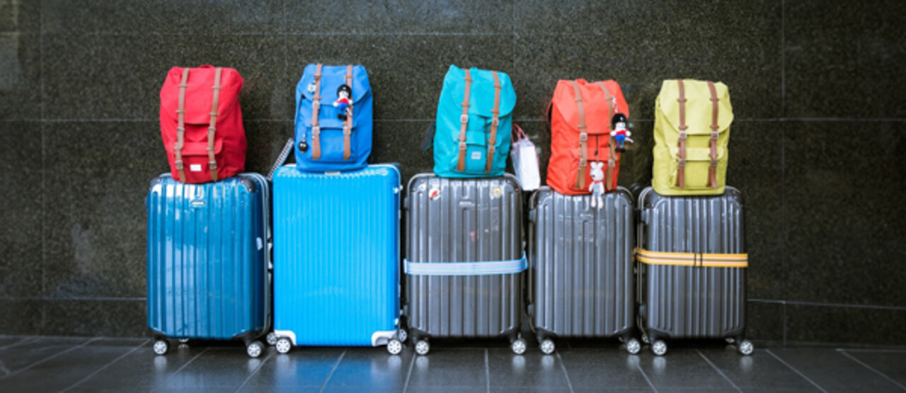 Bunte Kofferreihe mit draufgestellten Rucksäcken
